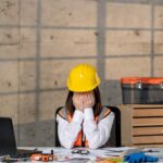 Femme qui à la tête dans les mains à son bureau et qui fait face à la complexité des travaux de rénovation.